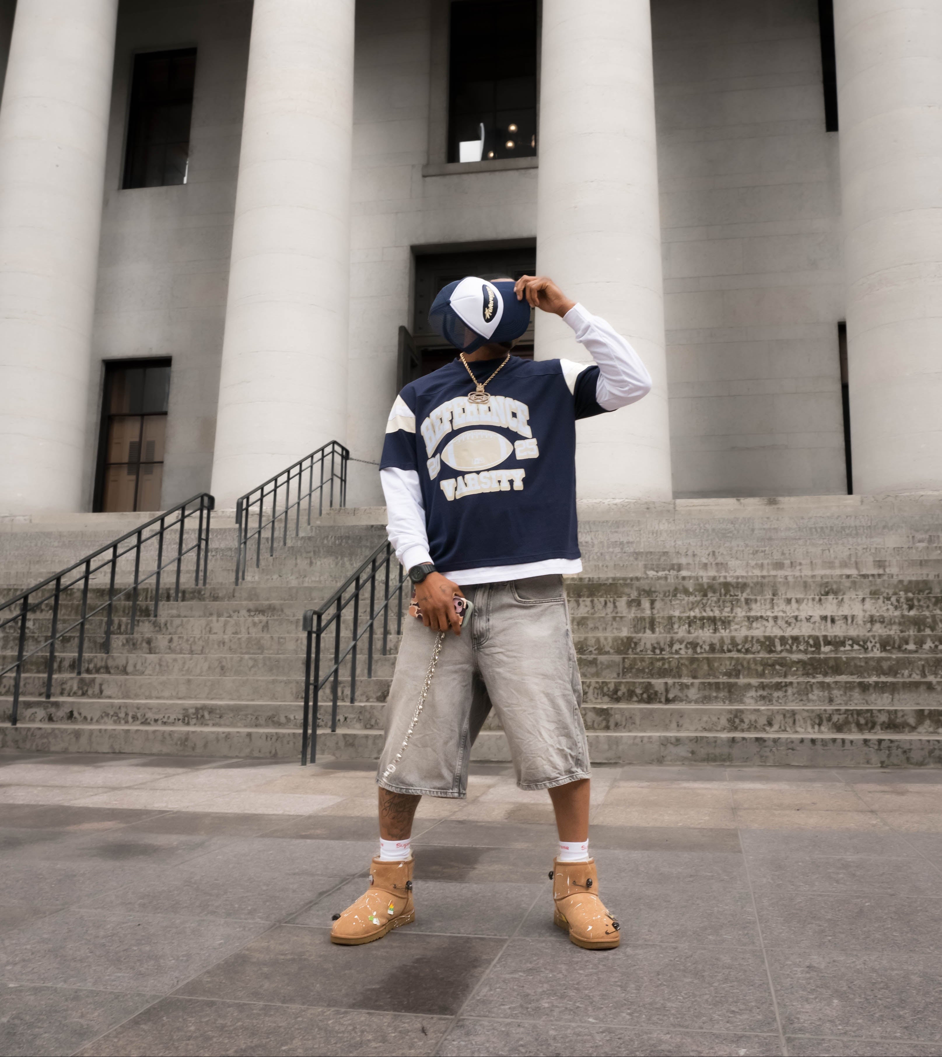 Person wearing a navy blue and white varsity jacket in front of a classical building with columns.